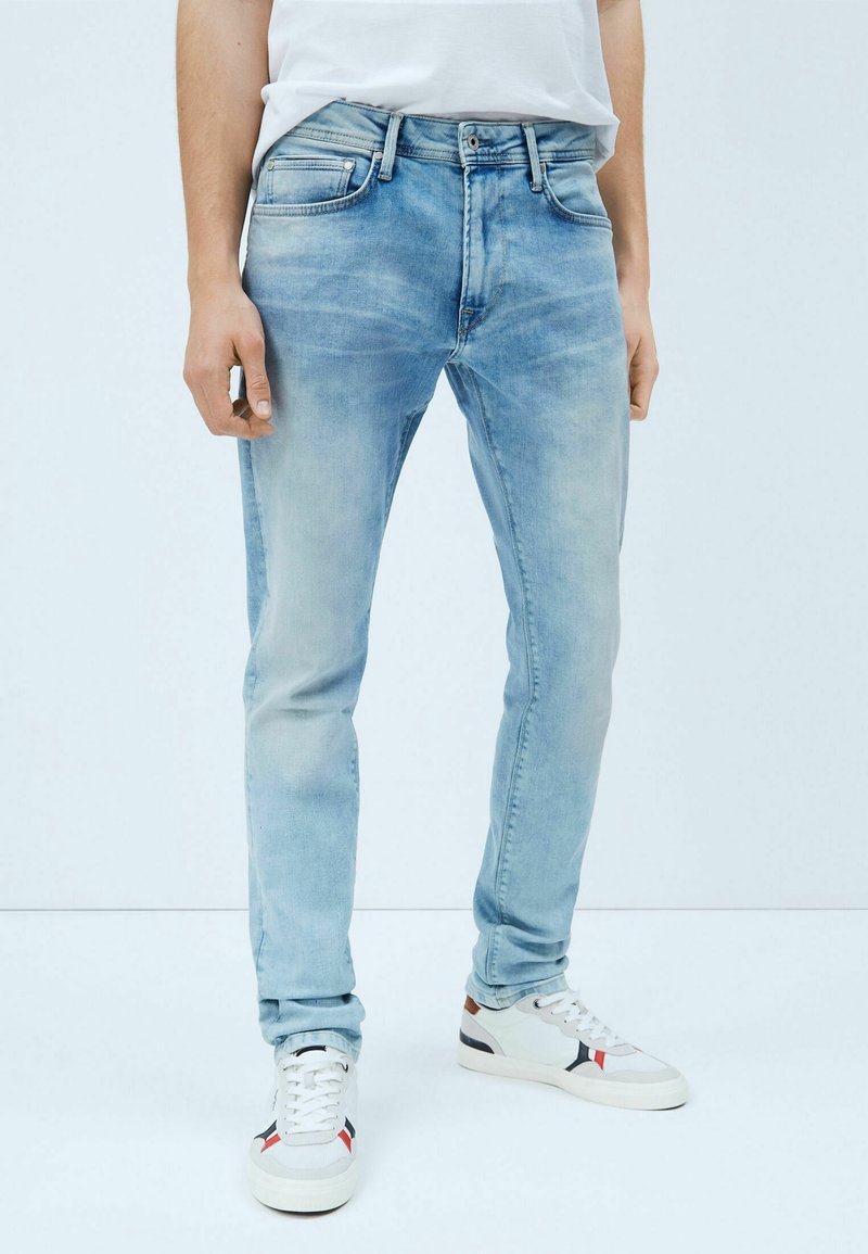 Vaaleansiniset farkut slim fit -mallilla, viidellä taskulla ja haalistuneella pesulla. Yhdistetty valkoisiin lenkkareihin, joissa on punaisia ja laivastonsinisiä yksityiskohtia.