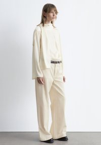 Cream-colored, long-sleeve top with a mock neckline and matching wide-leg corduroy pants. Features a black belt. Smooth texture, minimal design.