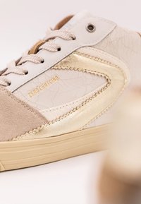 Sneaker med vit sprucken läder, beige mockadetaljer och guldmetalliska inslag. Har runda snören och präglad logotyp i guld.