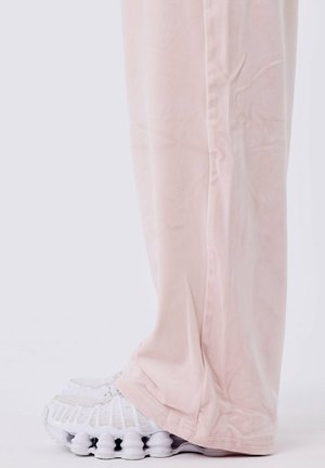 Lichtroze wijde broek van zacht materiaal, gecombineerd met witte sneakers met een gestructureerde zool en een mesh ontwerp op de bovenkant.
