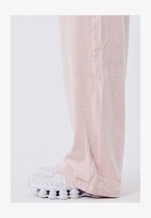 Pantalons larges rose clair en tissu doux, associés à des baskets blanches avec un sole texturé et un design en maille sur le dessus.
