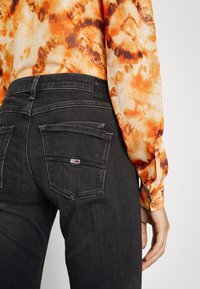 Svarta denimjeans med en figurnära design, som har framträdande bakfickor och sömmar. Bärs med en blus i orange tie-dye.