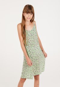 Bloemenpatroon jurk met een groene achtergrond en witte en zwarte bloemen, gemaakt van zachte stof, met een relaxte pasvorm en spaghettibandjes.