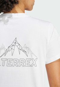 Bílá bavlněná tričko se geometrickým designem hory a nápisem "TERREX" v tučném černém písmu na zadní straně.