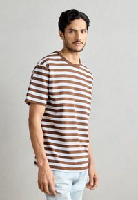 Brun og hvit stripete T-skjorte med kort erme og rund hals, teksturert stoff, med en avslappet passform. Brukes med lyseblå jeans.