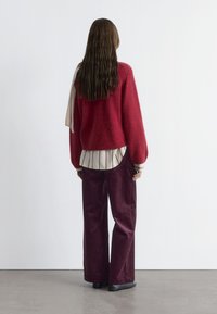 Red wool blend sweater with loose fit, paired with a cream and black striped shirt and burgundy corduroy wide-leg pants. Black shoes.