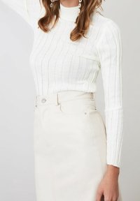 Witte ribgebreide trui met een hoge hals en lange mouwen, gecombineerd met een hoogwaisted beige rok met een voorklep en metalen knoop.