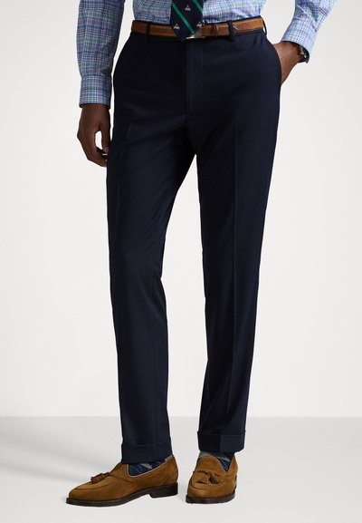 Navy trousers made of a smooth fabric, featuring a straight cut and subtle crease. Paired with brown suede loafers and patterned socks.