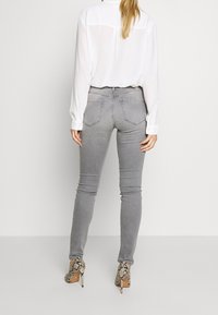 Jeans ajustados grises con bolsillos traseros y una cintura de media altura, combinados con una camisa blanca y tacones altos de estampado de serpiente. Textura de tela suave.