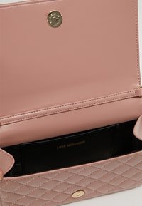 Peračník z prošívané růžové kůže se zlatými kovovými detaily, s uzávěrem na patent a černým interiérem, na kterém je vidět logo "LOVE MOSCHINO".