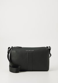 Sac bandoulière en cuir noir avec fermeture éclair, design plat, logo en relief et bandoulière ajustable. Texture lisse avec un minimum de détails.