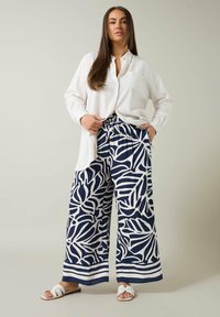 Camisa de lino blanca con un diseño de botones, combinada con pantalones anchos azul marino que presentan un patrón de hojas blancas y rayas horizontales en el dobladillo.