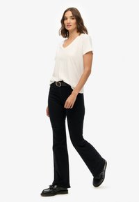 Camiseta blanca de cuello en V, pantalones flare negros, cinturón negro con hebilla redonda y zapatos negros. Diseño simple, corte relajado, textura suave.