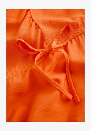 Orangefarbener Stoff mit einer glatten Textur, der mit einem gebundenen Schleifendetail und geraffter Naht versehen ist.