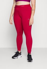 Leggings ajustés et taille haute d'un rouge vif avec un logo Tommy Hilfiger sur la ceinture. Texture lisse avec un matériau élastique et extensible.
