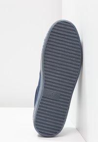 Námorně modrá podrážka boty s žebrovanou strukturou a průhlednou částí. Velikost označena jako 37 na tmavém povrchu.