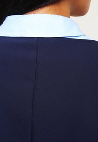 Nachtschwarz Kleid aus Stoff mit einem hellblauen Kragen, mit glatter Textur und sauberen Nähten, zeigt die Rückansicht und die Kragen-Details.