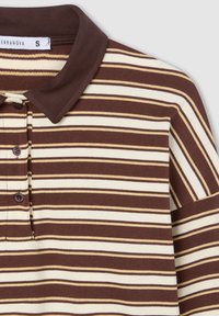 Polo a righe marrone e crema con una texture morbida, dotato di colletto e patta con tre bottoni. Maniche a taglio dritto e dettagli sottili.