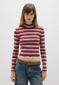 Langarm, cropped Oberteil mit gerippter Textur und horizontalen Streifen in Rosa und Braun. Mit Stehkragen. Kombiniert mit Jeans.