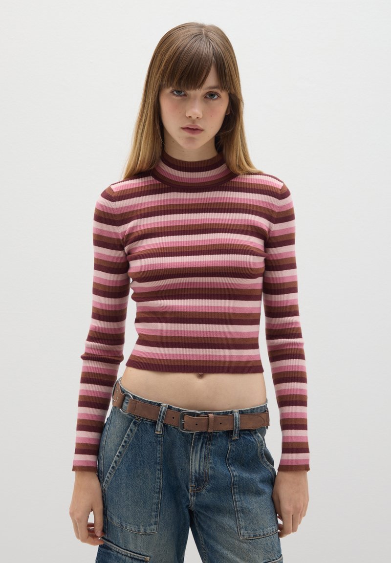 Langarm, cropped Oberteil mit gerippter Textur und horizontalen Streifen in Rosa und Braun. Mit Stehkragen. Kombiniert mit Jeans.