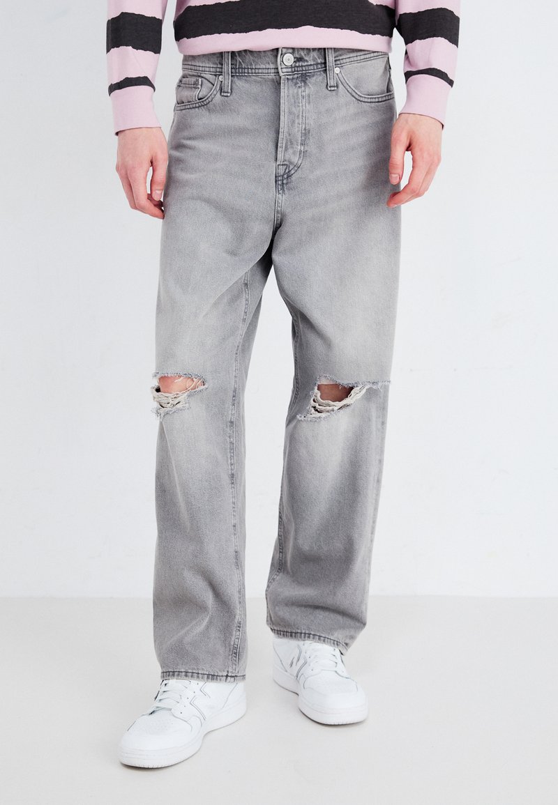 Jeans de denim gris claro con rodilleras desgastadas, con un diseño de pierna recta. Llevados con zapatillas blancas y un suéter a rayas.