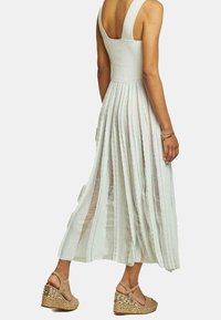 Abito maxi plissettato verde chiaro con spalline spesse e corpetto aderente. Indossato con sandali con zeppa beige caratterizzati da una texture intrecciata e dettagli in rilievo.