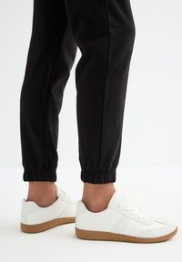 Zapatillas blancas de cuero texturizado, con suelas de goma marrón, combinadas con joggers negros con puños. Un diseño simple con acentos mínimos.