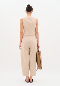 Top beige senza maniche e pantaloni a gamba larga realizzati in tessuto morbido; presenta un taglio corto, cuciture minime e una borsa a tracolla marrone coordinata.