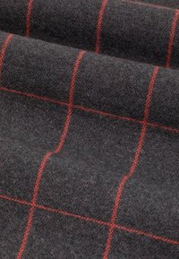 Szary wełniany materiał o miękkiej teksturze, z czerwonym kratkowanym wzorem. Materiał ma lekko puszysty wygląd, co potęguje wrażenie głębi.