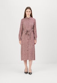 Rochie lungă cu imprimeu floral în tonuri de burgund, cu guler, închidere cu nasturi și talie legată. Modelul poartă pantofi cu toc înalt, negri.