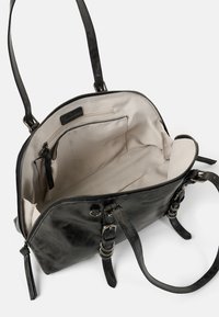 Sac à main en cuir noir à texture lisse, fermeture éclair et deux poignées. Intérieur avec doublure en tissu clair et plusieurs poches.