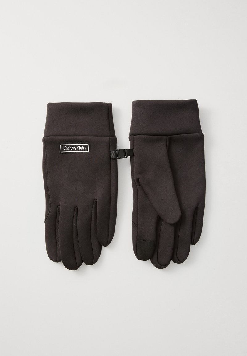 Schwarze Handschuhe aus einem weichen, glatten Stoff mit einem Logo-Patch und einem Riemen zur Sicherung. Die Finger sind verjüngt und besitzen eine touch-screen-kompatible Spitze.