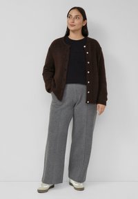 Ciemnobrązowy dziany kardigan z zapięciem na guziki, zestawiony z czarnym topem i jasnoszarymi szerokimi spodniami. Całość uzupełniona casualowym obuwiem.
