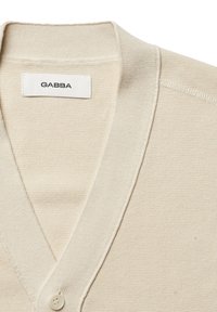 Béžový cardigan s výstrihom do V, textúrovanou tkaninou a jedným zapínaním na gombík. Štítok hovorí "GABBA."