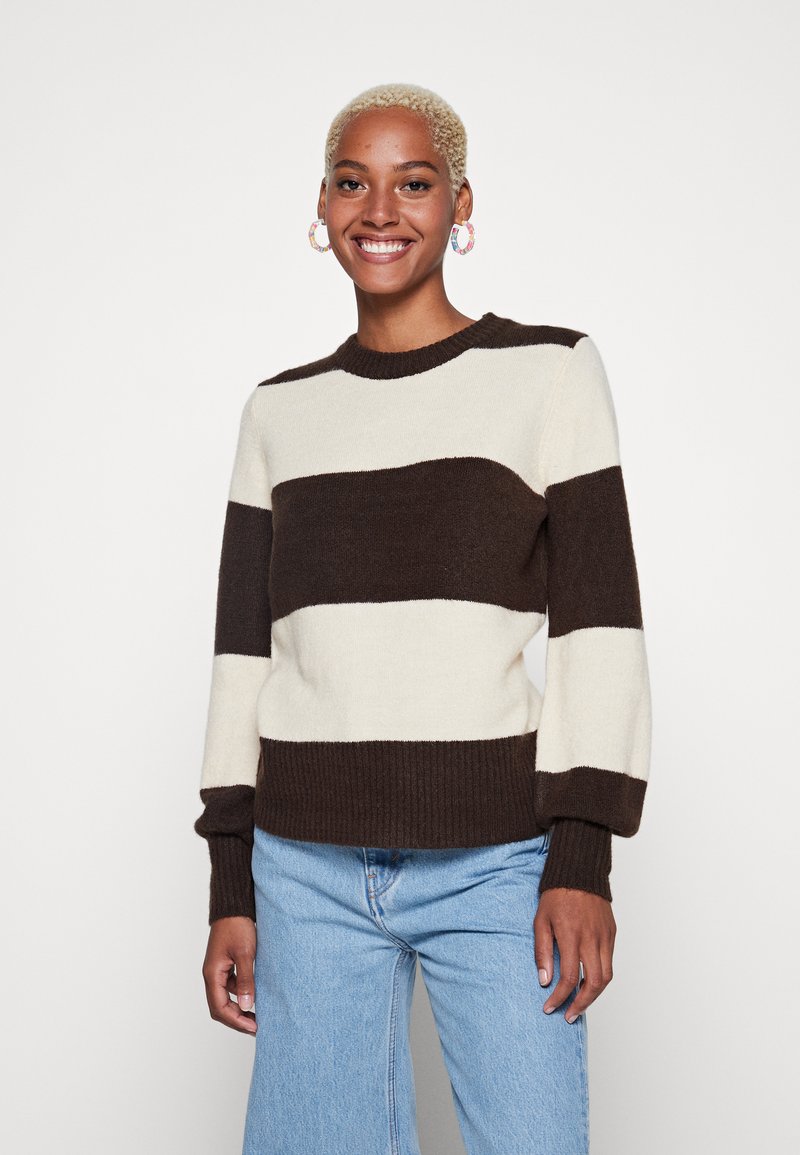 Pull en tricot avec de larges rayures crème et marron foncé, col rond, poignets et ourlet côtelés, associé à un jean bleu clair.
