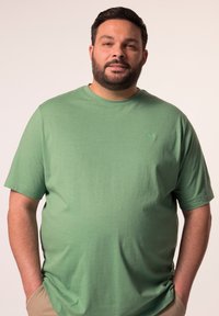 Zelené tričko s krátkým rukávem vyrobené z bavlny, s minimalistickým designem a malým logem na hrudi v uvolněném střihu.