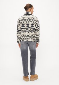 Pull en polaire crème avec des motifs géométriques bleu marine, col montant, manches longues, associé à un jean gris et des bottes beige.