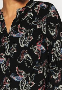Black blouse featuring intricate paisley pattern in red, blue, and white tones. Lightweight fabric, button detail, and a relaxed neckline.