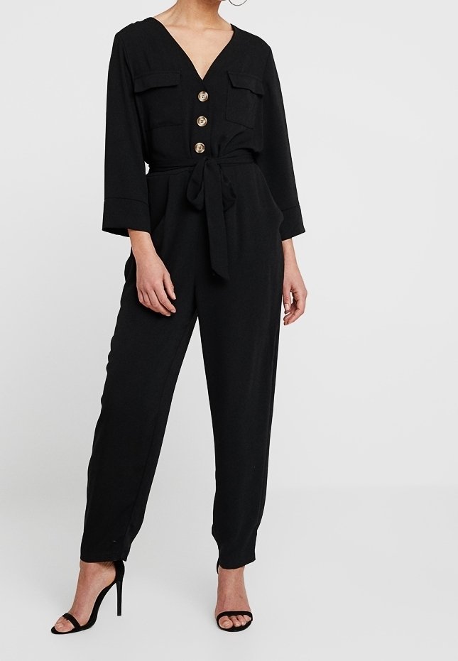 Svart jumpsuit med V-ringning, två framfickor, gulddetaljer, midjeband och avsmalnande ben. Bärs med svarta höga sandaler.