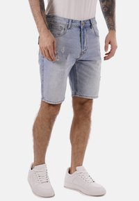 Shorts in denim blu chiaro con dettagli strappati, cinque tasche e una vestibilità classica. Abbinati a sneakers bianche per un look casual.