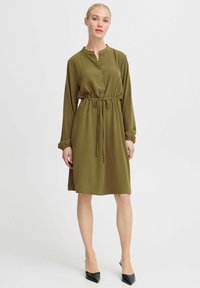 Olivgrön klänning med krage, knäppning fram, dragsko i midjan och långa ärmar, med ett mjukt tyg och knä-length design.