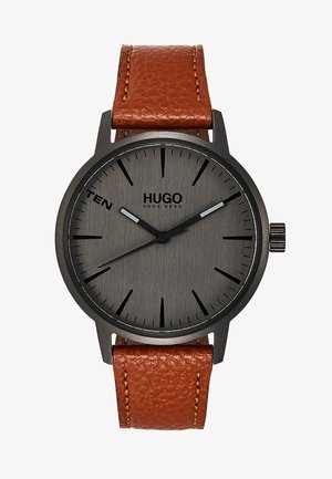 Rund sort metalur med mørkegrå urskive, sorte time markører, brun læderrem, teksten "TEN" ved kl. 10 og "HUGO BOSS" logo.