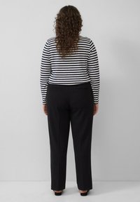 Gestreept top met lange mouwen in marineblauw en wit, gecombineerd met zwart op maat gemaakte broek. De outfit heeft een ontspannen pasvorm met een rechte pijp.