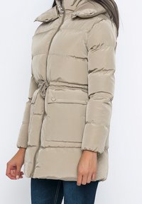 Beige gepolsterte Jacke mit hohem Kragen, Kordelzug in der Taille und Reißverschluss vorne. Verfügt über zwei Fronttaschen und elastische Bündchen.