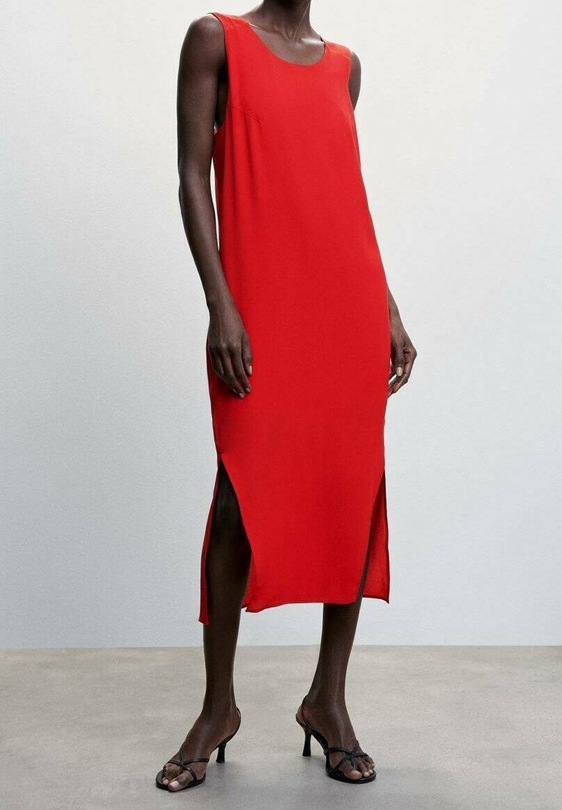 Robe sans manches rouge avec une silhouette droite, des fentes sur les côtés et un tissu lisse. Portée avec des sandales à lanières noires sur un fond neutre.