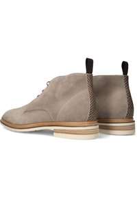 Beige suede enkellaarsjes met gestructureerde hakpanelen, bruine veters en contrasterende witte stiksels. Ronde neus en lage gestapelde hak.