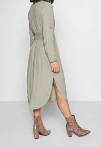 Olivgrön skjortklänning med bälte, långa ärmar och sidofickor, i kombination med bruna ankelboots i ormskinnsmönster med klack.