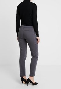 Pantalon gris sur mesure à coupe ajustée, avec une texture lisse, des poches latérales et une taille mi-haute, associé à des escarpins noirs.