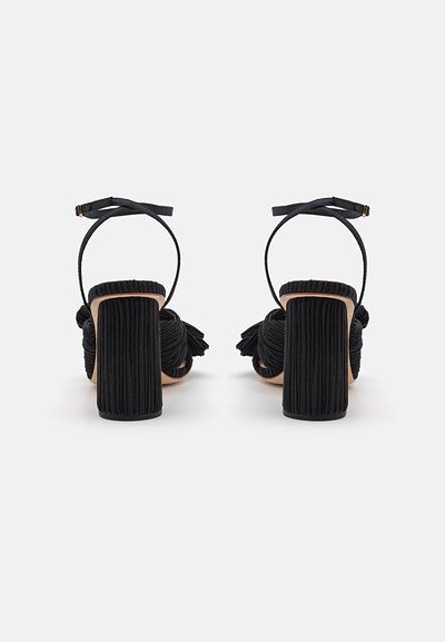 Sandalias de tacón negro con parte superior de tela texturizada, tacones de bloque y correas para el tobillo. Diseño plisado con acentos de borlas.