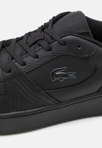 Must mustaga leather sneaker, mille struktuuriga pind, paeltega disain ja külje peal suur tume logo. Kummi välistald haarde jaoks.